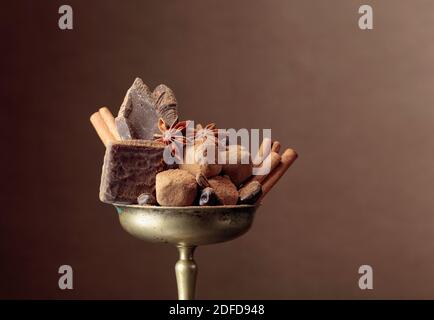 Vari cioccolatini con ingredienti. In una vecchia ciotola di ottone caramella, chicchi di caffè, cannella, anice e pezzi di cioccolato nero rotto. Spazio di copia. Foto Stock