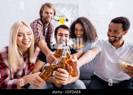 amici allegri multiculturali che sorseggiano bottiglie di birra in primo piano sfocato Foto Stock