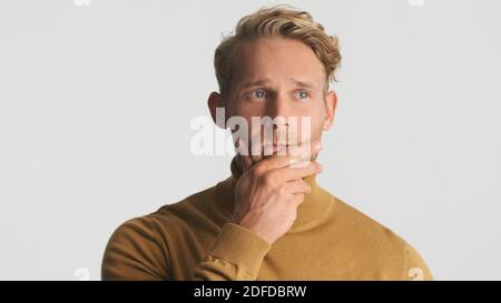 Giovane attraente uomo bearded tenere la mano sul mento pensare su telecamera isolata su sfondo bianco. Uomo pazzo Foto Stock
