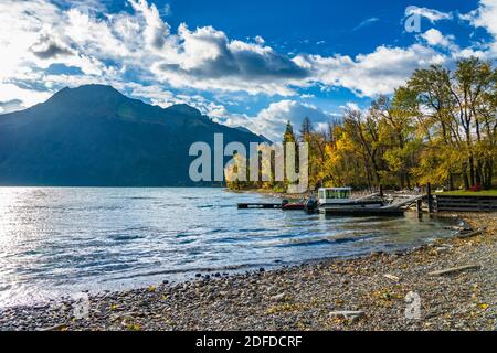 Waterton Middle Lake lancio barca in autunno fogliame stagione soleggiata giorno mattina. Luce del sole che passa il cielo blu e le nuvole sulle montagne. Parco dei laghi di Waterton Foto Stock