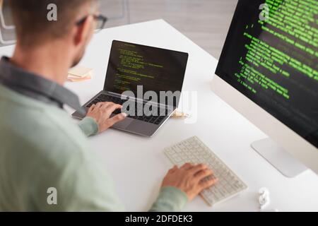 Vista posteriore del programmatore maturo seduto al tavolo in sviluppo su un computer desktop Foto Stock