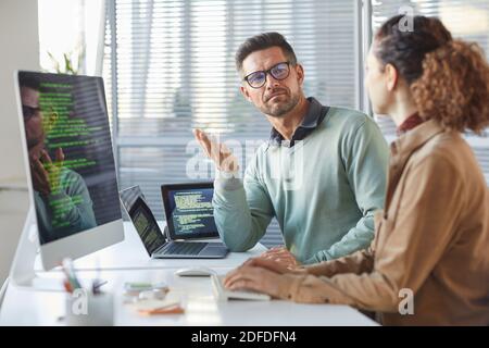 Due colleghi seduti al tavolo davanti ai computer E discutere del nuovo software nell'ufficio IT Foto Stock