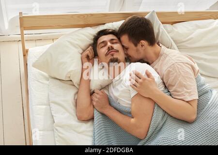 Felice coppia gay sdraiata sul letto a casa vista da sopra Foto Stock