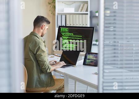 Tecnico maturo seduto sul posto di lavoro davanti al computer Monitoraggio e digitazione sul computer portatile dell'ufficio IT Foto Stock