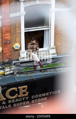 Un uomo seduto sul davanzale che fuma, Electric Avenue, Brixton, Londra Foto Stock