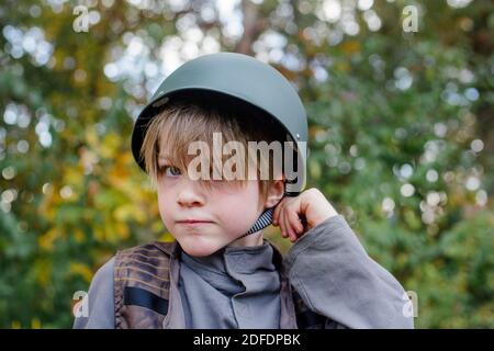 Un ragazzo vestito con un soldato in costume si toglie al cinghia del suo casco Foto Stock