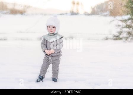 Adorabile bambino in piedi nella neve in fattoria indossando lana lavorato a maglia vestiti Foto Stock