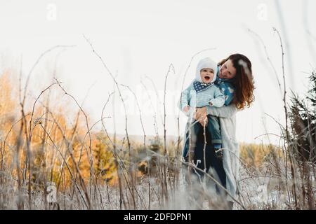 Madre che tiene il bambino in armi in una giornata di sole dentro campo ghiacciato invernale Foto Stock