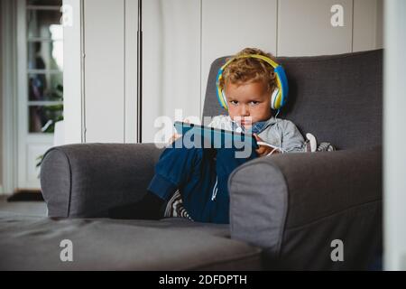 Ragazzo che inpouisce giocando con un tablet e indossando le cuffie a. casa covid Foto Stock