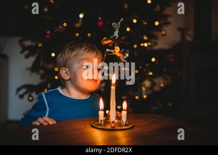 Bambino che soffia candele da un ornamento natalizio con un albero dietro Foto Stock