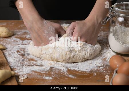 Giovane bella donna impastare impasto ad un tavolo di legno in cucina. Hobby casalinga concetto. Foto Stock