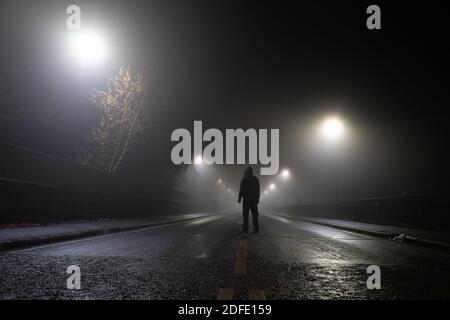 Angolo basso, guardando in su una figura agganciata che si trova nel mezzo della strada in una notte d'inverno foggy atmosferica. REGNO UNITO. Foto Stock