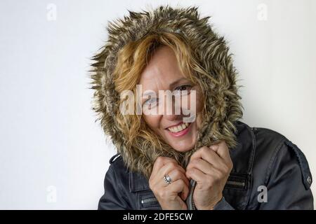 Donna bionda di mezza età completamente coperta in una giacca con un cappuccio in pelliccia, ripara dal freddo e dal vento Foto Stock