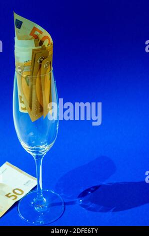 Bicchiere di vino frizzante riempito con banconote, fondo blu. Foto Stock