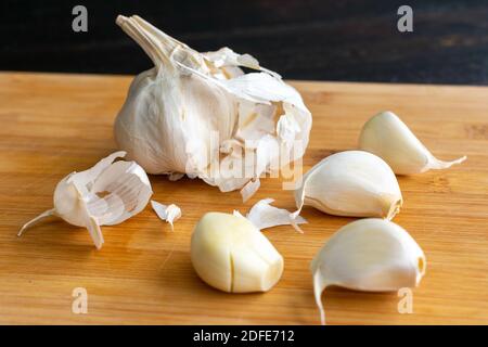 Primo piano di spicchi d'aglio: Spellatura e smashing spicchi d'aglio su un tagliere di bambù Foto Stock