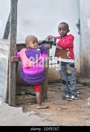 Ranohira, Madagascar - 29 aprile 2019: Due bambini malgascio sconosciuti in piedi da un mercato di legno vuoto stallo sulla strada, guardando in macchina fotografica, un masticare Foto Stock