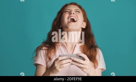 Bella ragazza eccitata gridando mentre emotivamente giocare in gioco su smartphone su sfondo colorato Foto Stock