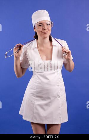 giovane donna dottore in un cappotto bianco e cappello in posa su sfondo blu Foto Stock