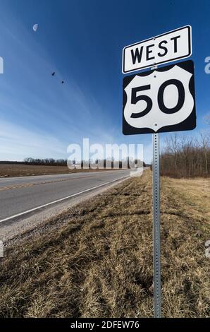 Un'indicazione stradale sul lato della US-50 fuori Brownstown, IN. Un primo quarto di luna e gru di sandhill volanti sono sullo sfondo. Foto Stock