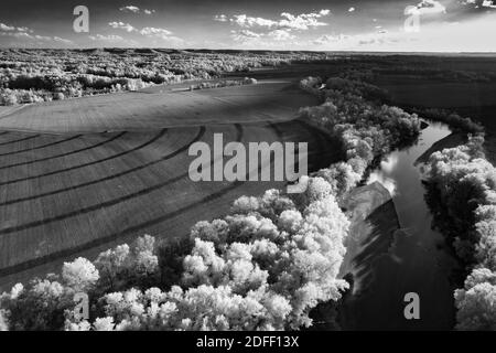 Una foto aerea a infrarossi in bianco e nero di un campo con un fiume fiancheggiato da alberi. Ci sono alcuni semi-cerchi formati da pneumatici di un irrigatore di campo. Foto Stock