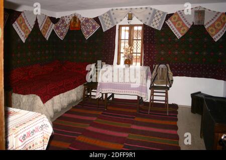 Village Museum, Bucarest, Romania. Interno di una vecchia casa tradizionale in legno, con mobili semplici e arazzi fatti a mano e decorazioni. Foto Stock