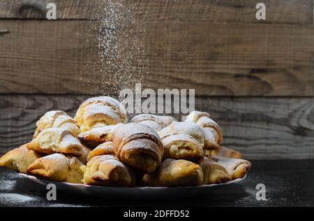 Biscotti fatti in casa sotto forma di bagel con marmellata di ripieno cosparso di zucchero in polvere su uno sfondo di legno. Messa a fuoco selettiva. Foto Stock