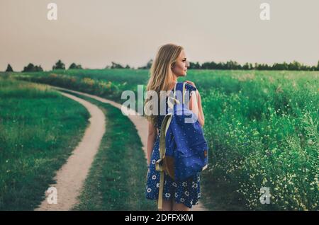 donna si trova in un abito e uno zaino al centro Di un campo verde su un sentiero Foto Stock