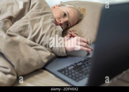 La ragazza adolescente si trova a letto e lavora su un computer portatile. Alta qualità Foto Stock