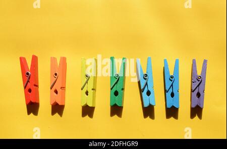 Sette spicchi di legno multicolore, dipinti nei colori dell'arcobaleno, su sfondo di carta giallo, giacciono in fila. Foto Stock