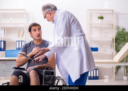 Paziente giovane di sesso maschile in sedia a rotelle che visita il radiologo medico anziano Foto Stock