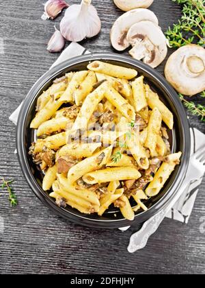 Penne con funghi selvatici in un piatto su un asciugamano da cucina, timo, forchetta e aglio su sfondo di legno dall'alto Foto Stock