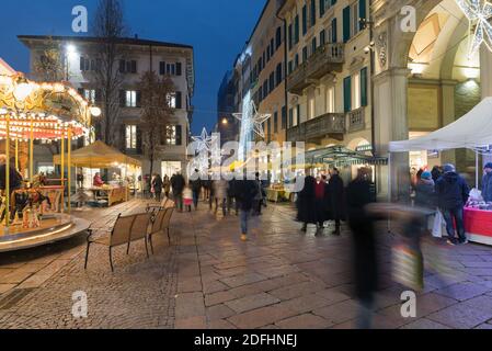 Mercatino di Natale in serata e folla di persone sulla strada di una città con luci di natale. Centro storico di Varese, corso Matteotti, Italia Foto Stock