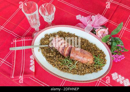 Cotechino (salsiccia di maiale) con lenticchie. Piatto tradizionale italiano. Sfondo con tovaglia rossa Foto Stock