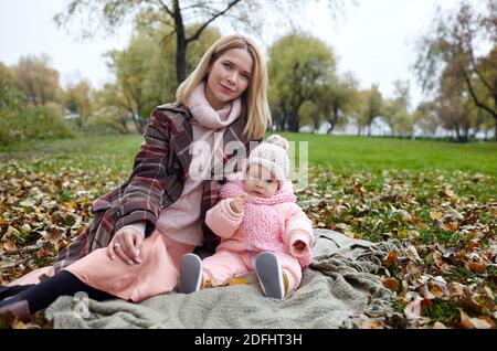 Bella bambina con madre seduta sulla plaid. Famiglia all'aperto. Adorabile bambina in abiti caldi al pic-nic in autunno parco il giorno di sole. Foto Stock