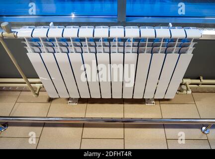 Moderno radiatore di riscaldamento bimetallico installato sotto una finestra in un edificio industriale Foto Stock