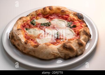 Pizza di Napoli, chiamata margherita perché dedicata alla regina - pizza croccante, pomodoro, mozzarella e basilico in piatto bianco Foto Stock