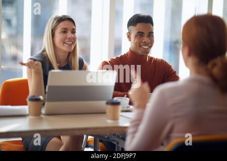Una giovane candidata che ha un colloquio per un lavoro con una commissione aziendale in un'atmosfera piacevole. Persone, lavoro, azienda, business concept. Foto Stock