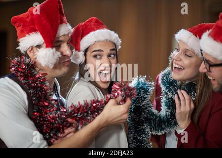 Un gruppo di colleghi eccitati che gridano e posano per una foto alla festa di Capodanno nel corridoio in un'atmosfera di vacanza sul posto di lavoro. Insieme, ne Foto Stock