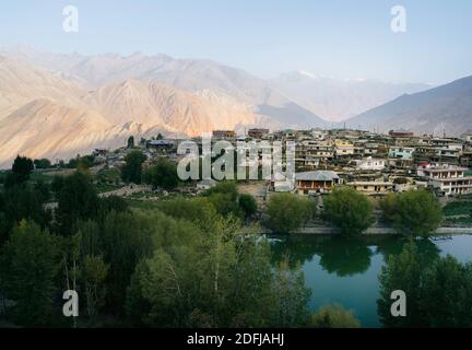 Villaggio fiancheggiato da campi, lago, alte montagne dell'Himalaya, e alberi nella valle di Spiti all'alba a Nako, Himachal Pradesh, India. Foto Stock