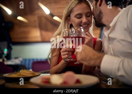 giovane uomo caucasico con barba che sussurra a biondo attraente a cena romantica in ristorante Foto Stock