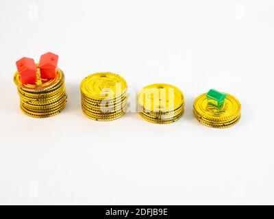 Un insieme di piccole case di colore rosso circondate da monete d'oro. Concetto di bene immobile, investimento e consumo. Foto Stock