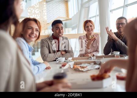 Un gruppo di dipendenti in una pausa gustando chatt e cibo in un'atmosfera allegra presso la mensa dell'azienda. Persone, lavoro, azienda, business concept. Foto Stock