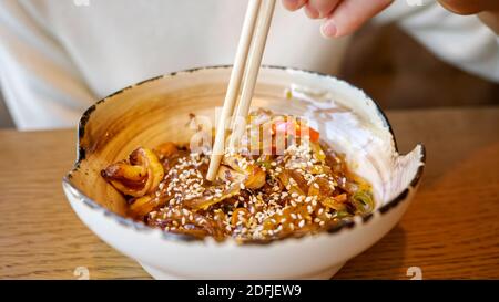 Donna irriconoscibile che mangia tagliatelle trasparenti con pesce in un caffè. Foto Stock