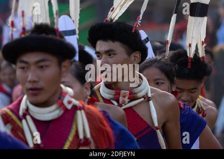 Giovani tribesi Naga che indossano abiti tradizionali nell'arena centrale di Kisama Village a Nagaland India il 2 dicembre 2016 Foto Stock