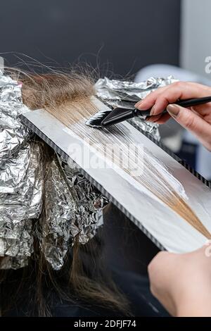 Stylist dei capelli che applica la polvere sbiancante sui capelli del cliente e che avvolge nella lamina. Tecnica di shatush Foto Stock
