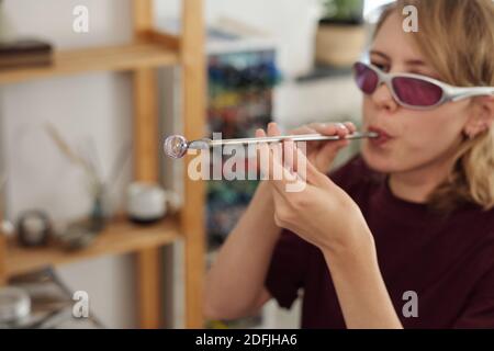 Le mani di giovane donna esperta lavoratrice padrone in casualwear e. occhiali protettivi che soffiano nel tubo lungo in officina Foto Stock