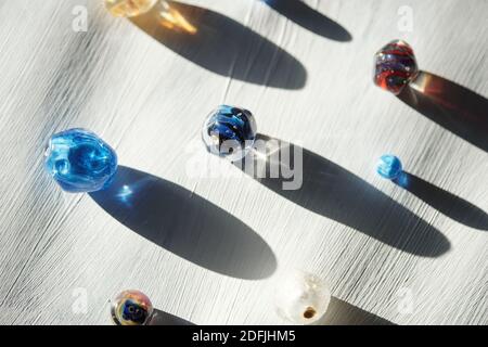 Gruppo di perle di vetro di vari colori e forme e. le loro lunghe ombre su tavola di legno dipinte in bianco che può essere utilizzato come sfondo Foto Stock