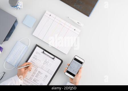 Panoramica del medico passa il modulo cronologico durante lo scorrimento attraverso i dati nello smartphone e controllarli dall'ambiente di lavoro Foto Stock