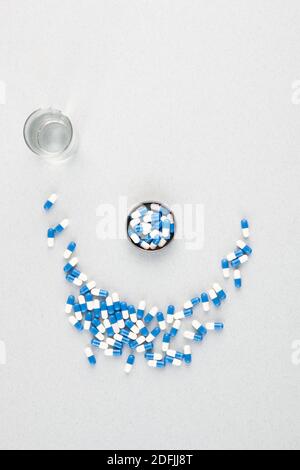 Panoramica di piccolo vaso contenente pillole blu-e-bianco e mucchio di loro che formano il sorriso che termina in vetro di acqua con copyspace tutto intorno Foto Stock
