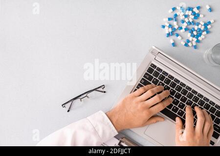 Panoramica delle mani di un medico contemporaneo che si riempie di medicina elettronica documenta mentre tocchi i tasti della tastiera del computer portatile dal luogo di lavoro Foto Stock